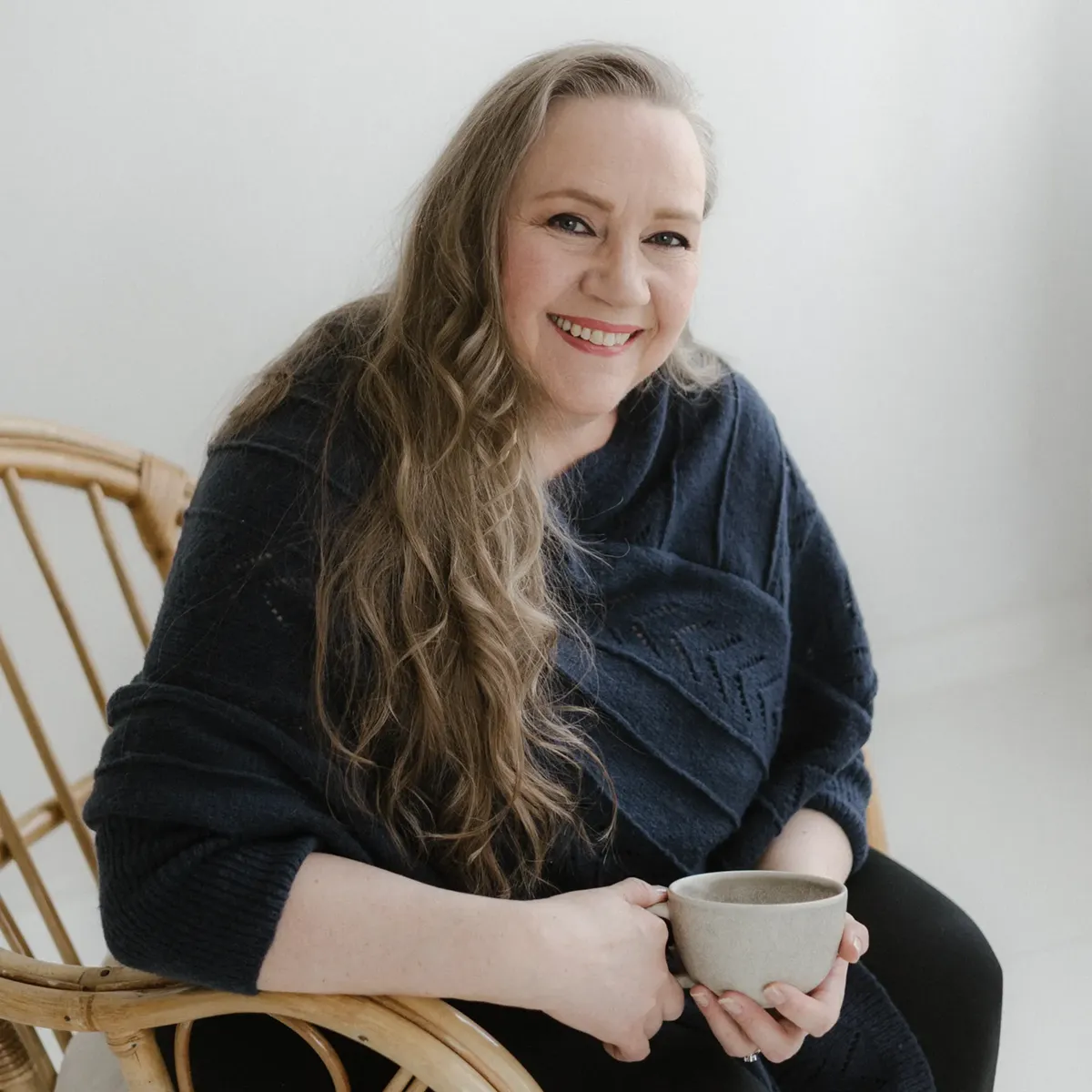 Tarja Sassi istuu hymyillen kahvikuppi kädessä valoisassa huoneessa. Hänellä on yllään tummansininen neule.