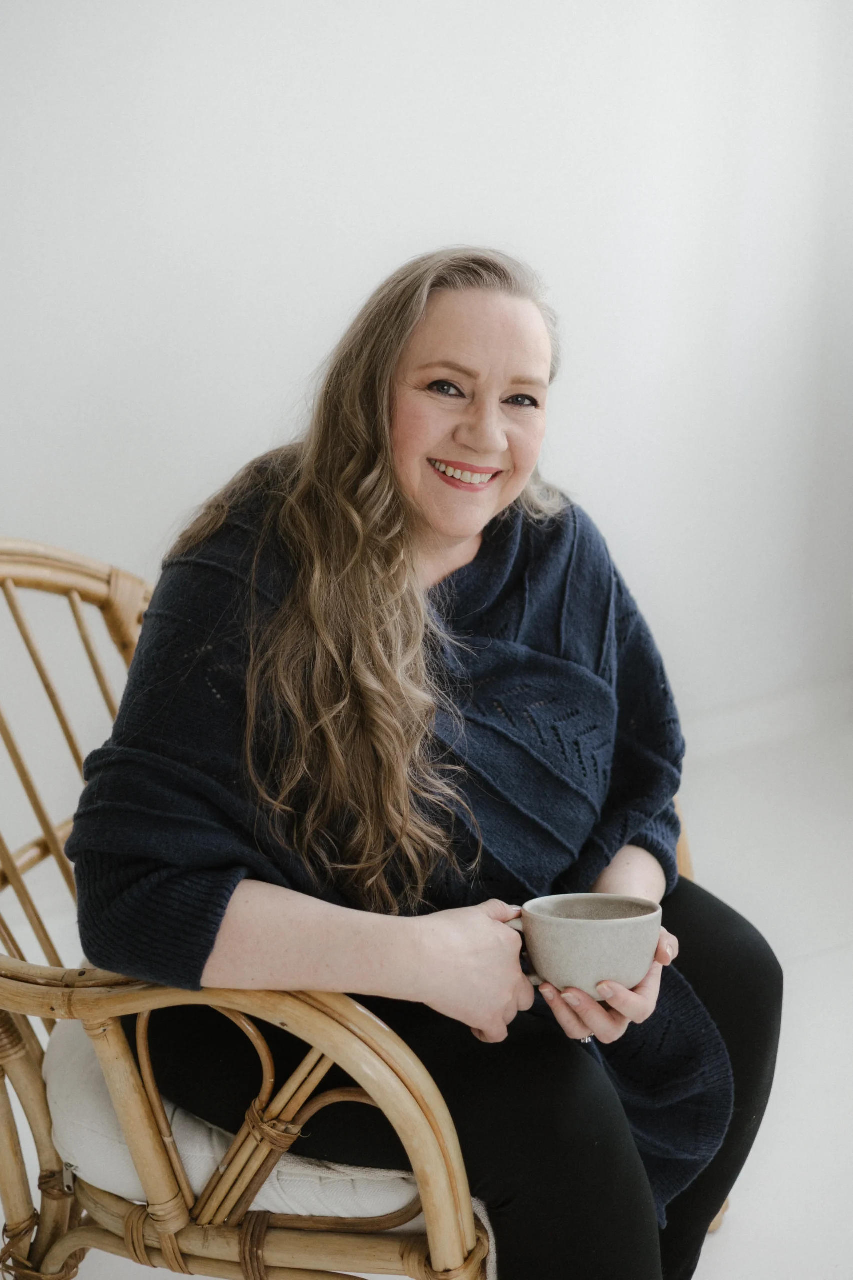 Tarja Sassi istuu hymyillen kahvikuppi kädessä valoisassa huoneessa. Hänellä on yllään tummansininen neule.