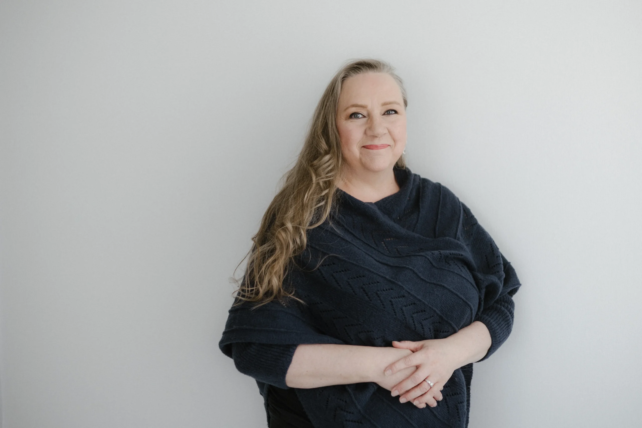 Tarja Sassi seisoo hymyillen valoisassa huoneessa. Hänellä on yllään tummansininen neule.